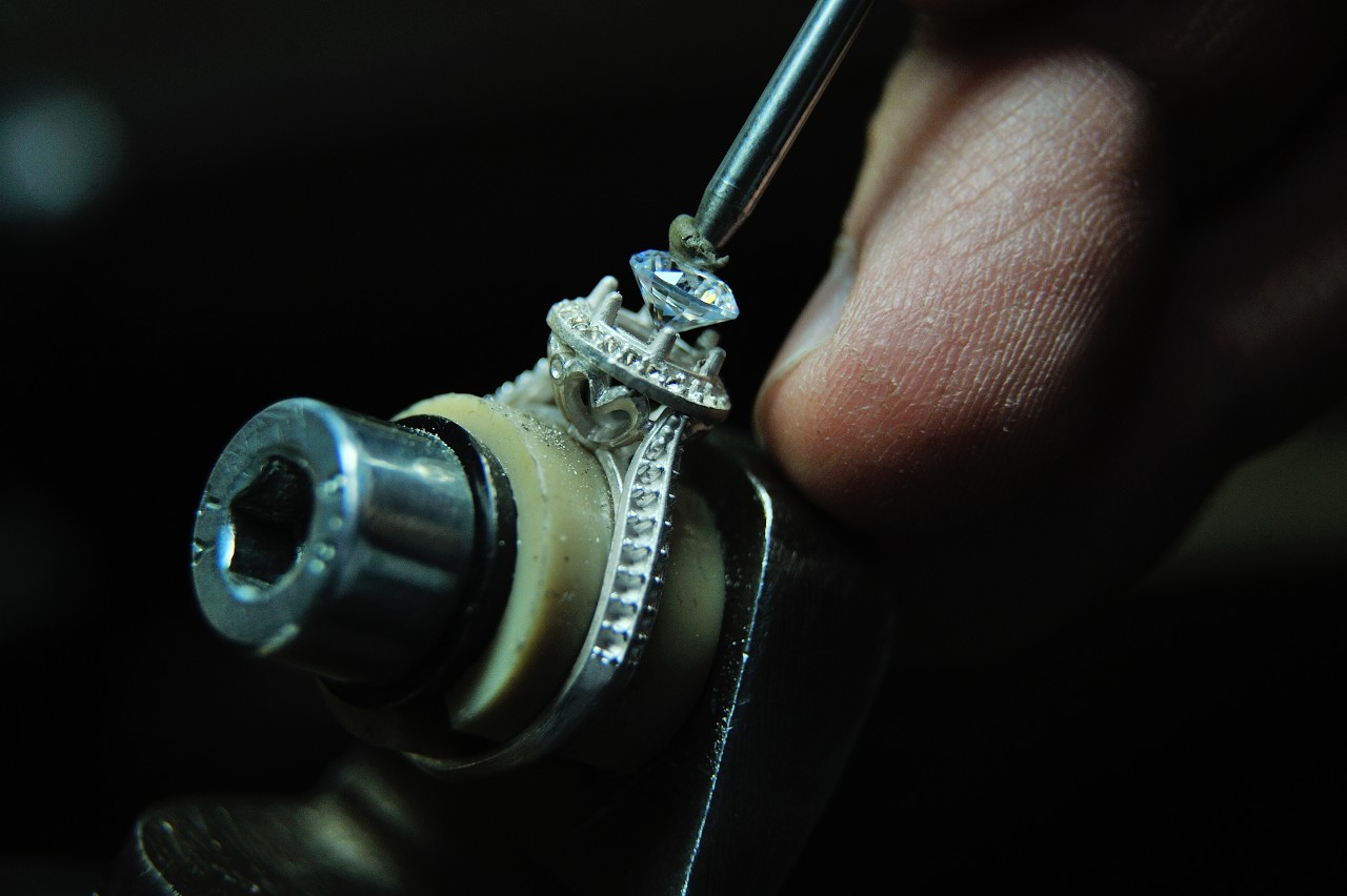 A jeweler sets a diamond in a ring setting in a dark workshop.
