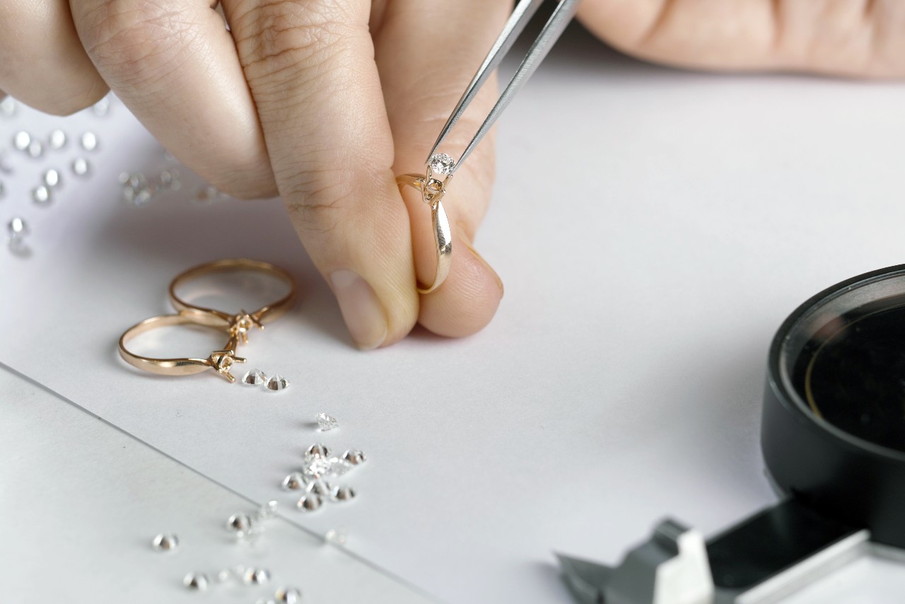 A jeweler chooses a diamond to set into three solitaire engagement rings.