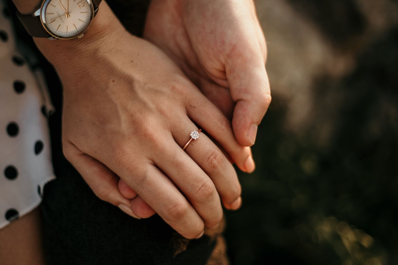 close up image of a couple’s hands holding each other – the woman’s hand wearing an engagement ring