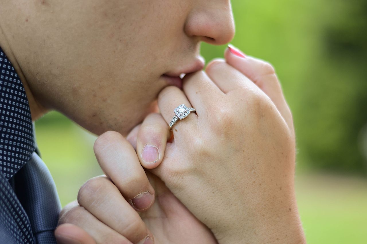 a man kissing the hand of his fiancee who is wearing a halo, sidestone engagement ring