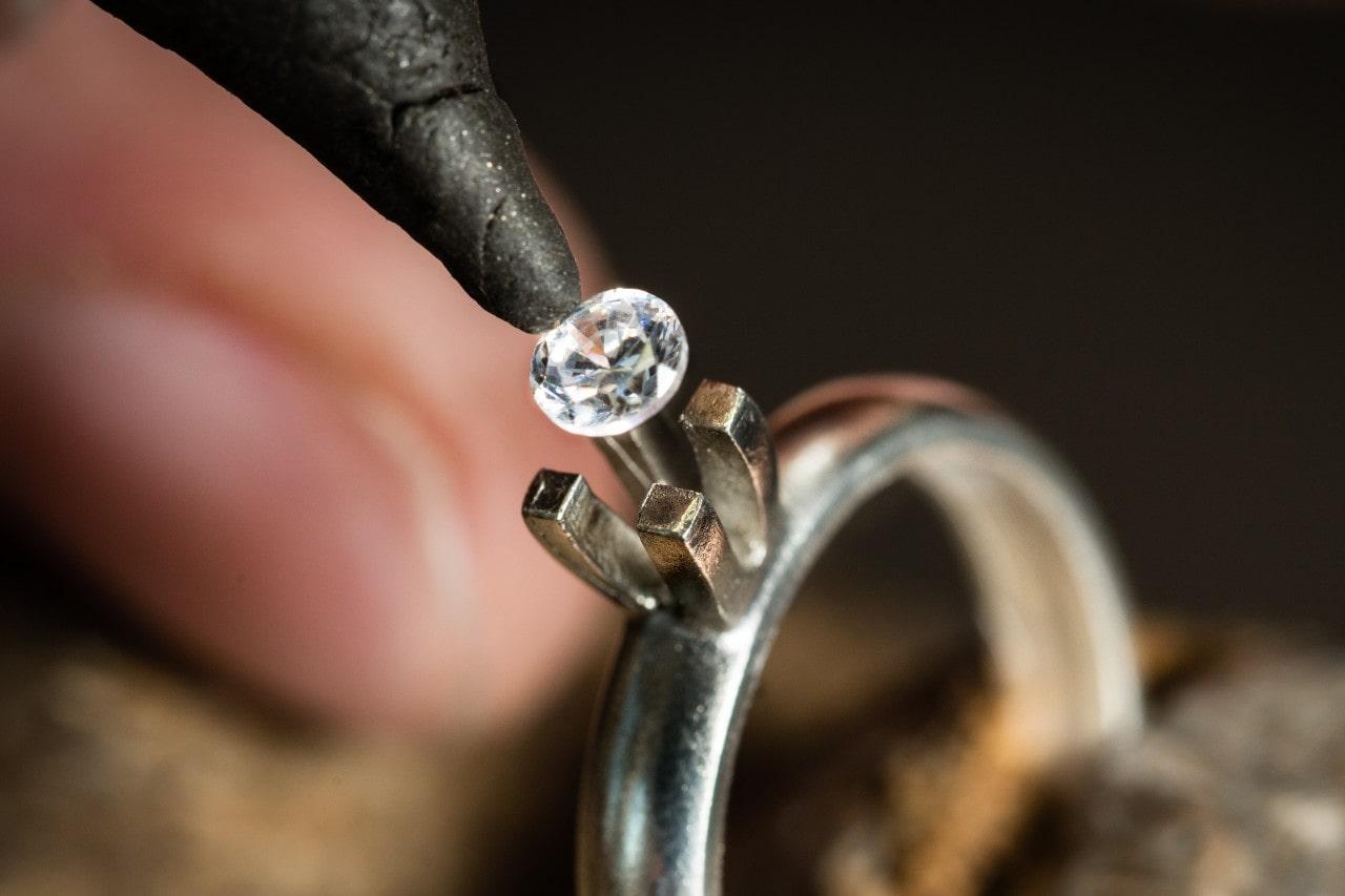 A jeweler setting a round cut diamond into a prong setting of a white gold solitaire setting
