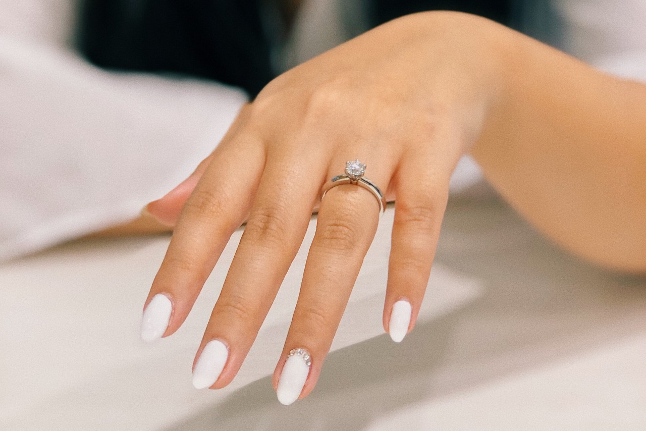 An outstretched hand with white nails wearing a solitaire round cut engagement ring