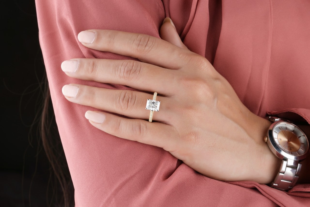 Woman in a pink shirt wearing a gold, emerald cut engagement ring