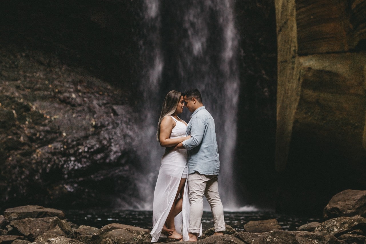 a couple embraces in front of a waterfall.