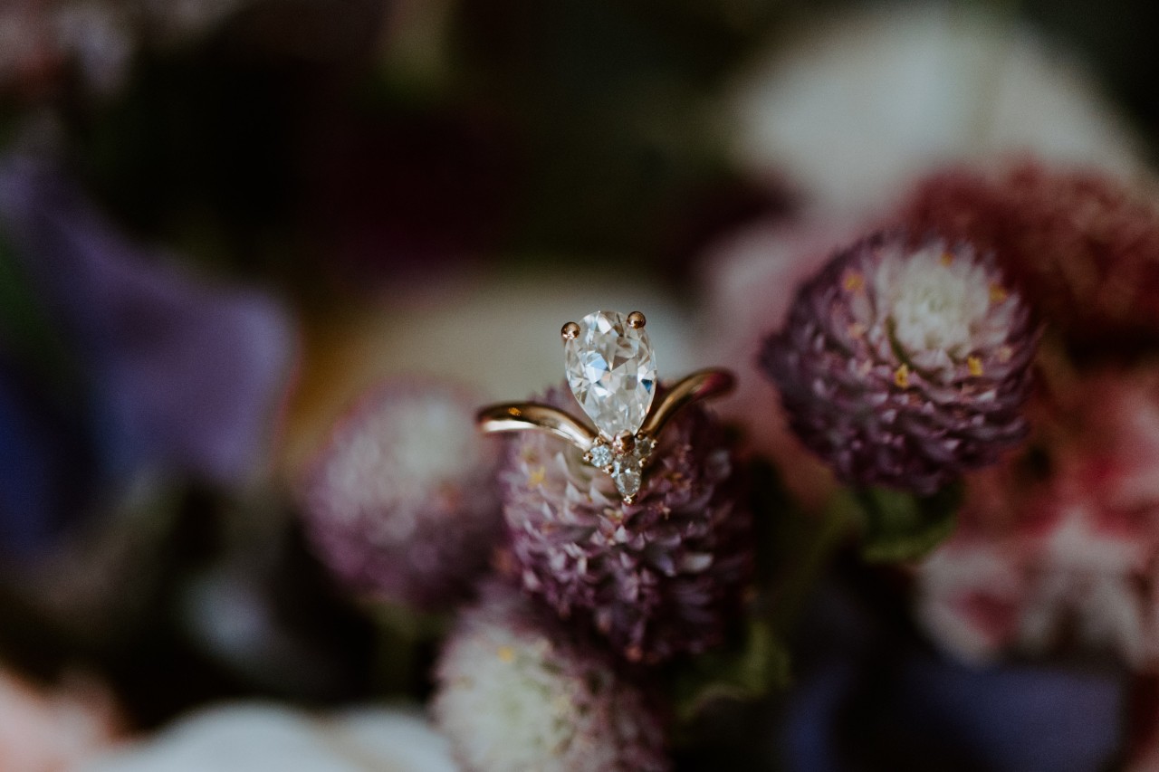 a pear shape engagement ring sitting on a purple flower