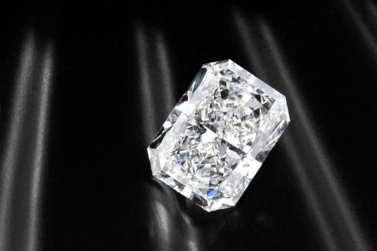 A close-up of a shining cushion cut diamond on a sleek black fabric backdrop.