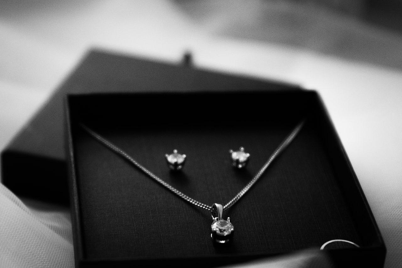 A black and white close-up of a jewelry set featuring diamond stud earrings and a matching pendant necklace.