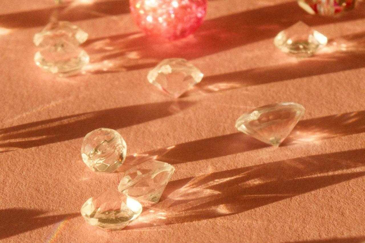 A brightly lit close-up of seven round cut diamonds brilliantly refracting light onto a textured coral-colored backdrop.
