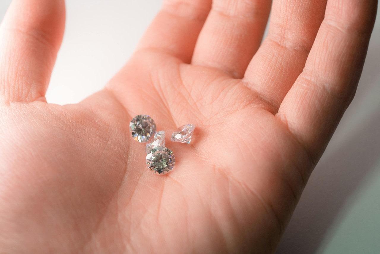 A close-up of a person’s hand with four stunning round cut diamonds resting in their palm.