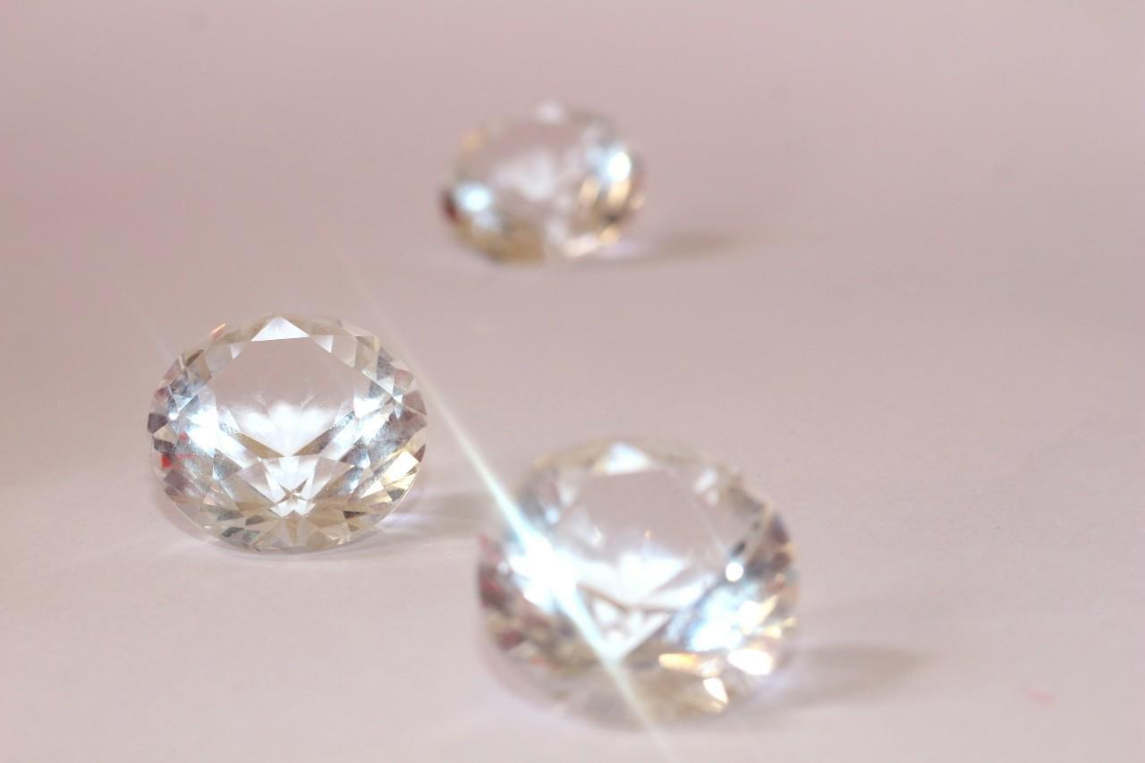 A close-up of three round cut diamonds shining on a soft pink backdrop.