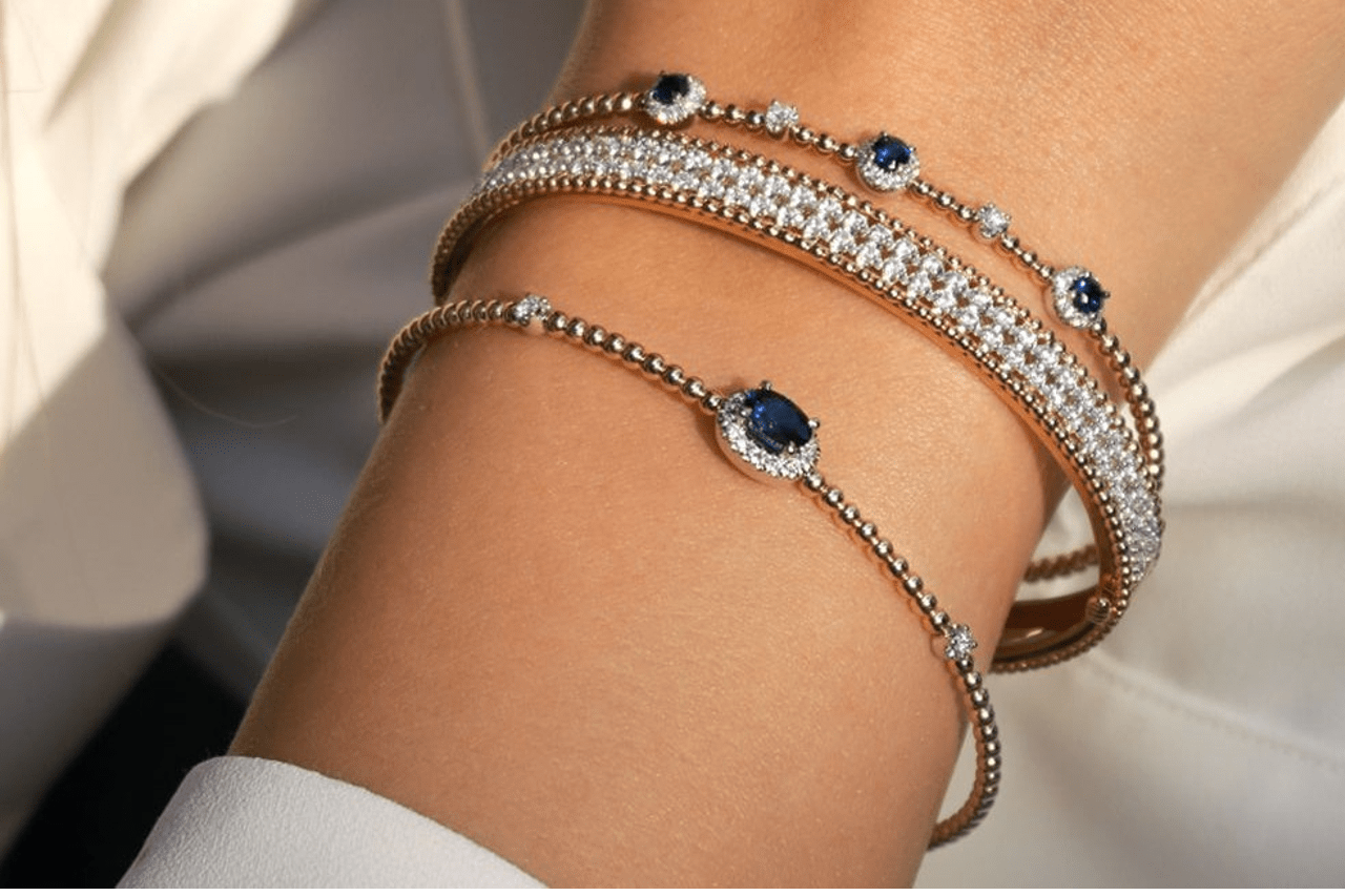 close up image of a woman’s wrist adorned with three mixed metal bracelets featuring diamonds and blue sapphires
