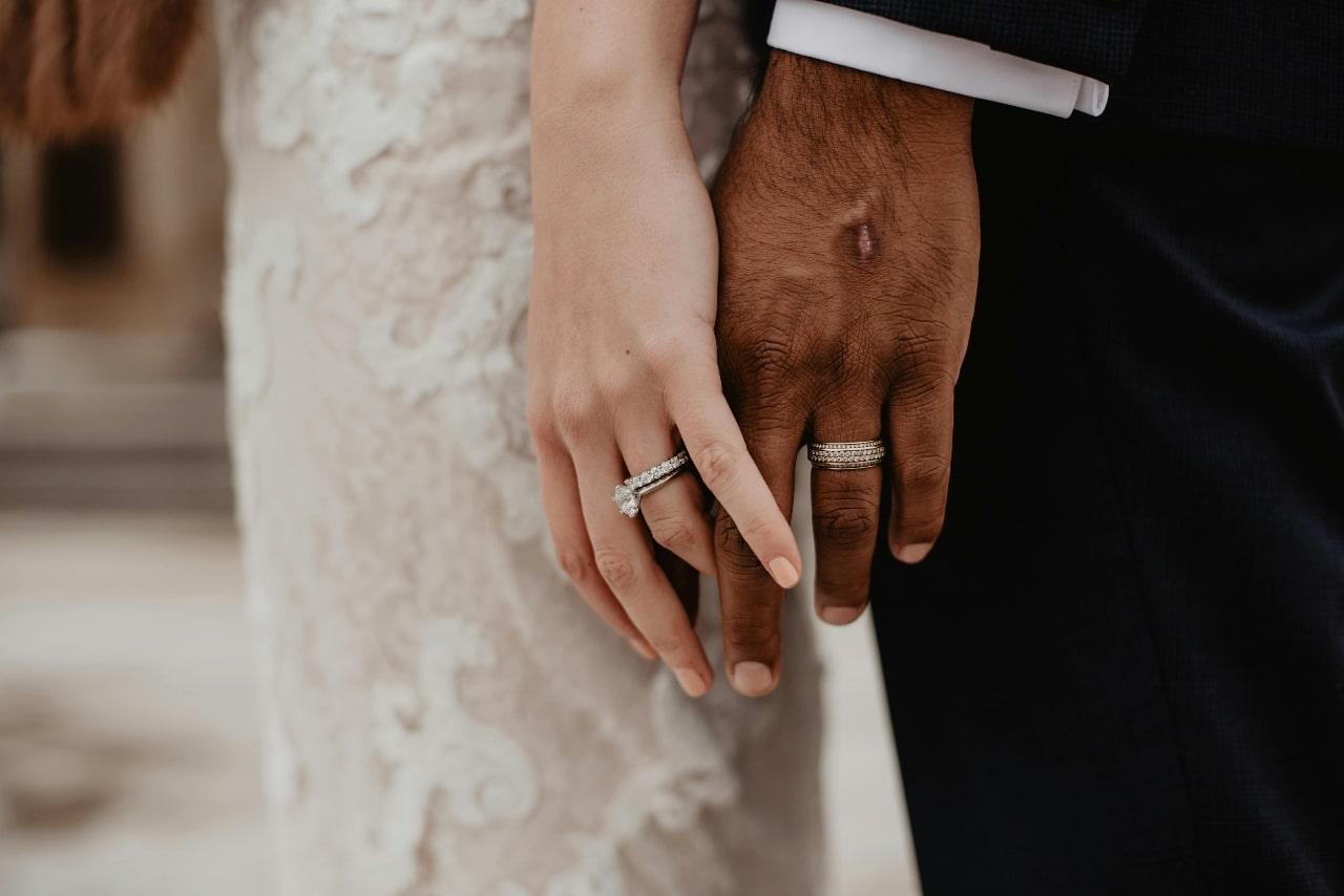 A bride and groom holding hands, the bride wearing a white gold engagement ring.