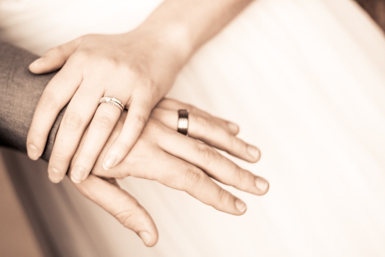 A newlywed couple holding hands showcasing a yellow gold wedding band and engagement ring.