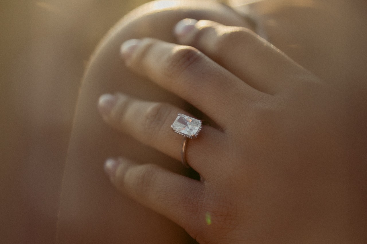 a woman’s hand resting on her shoulder, wearing a radiant cut solitaire engagement ring