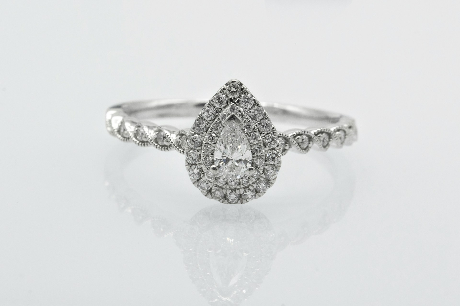 a white gold engagement ring with a pear shape center stone and halo setting