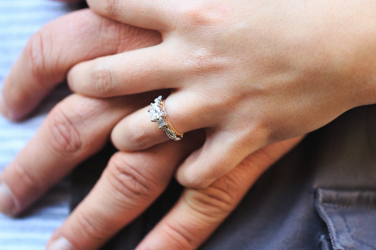 a couple’s hands intertwined, the woman’s hand adorned with a mixed metal engagement ring