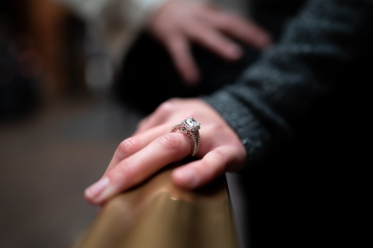close up image of a person’s hand resting on a rail and wearing an elaborate engagement ring