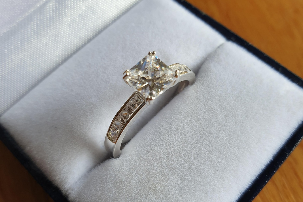 A white gold side stone diamond engagement ring with a princess cut diamond inside the white jewelry box