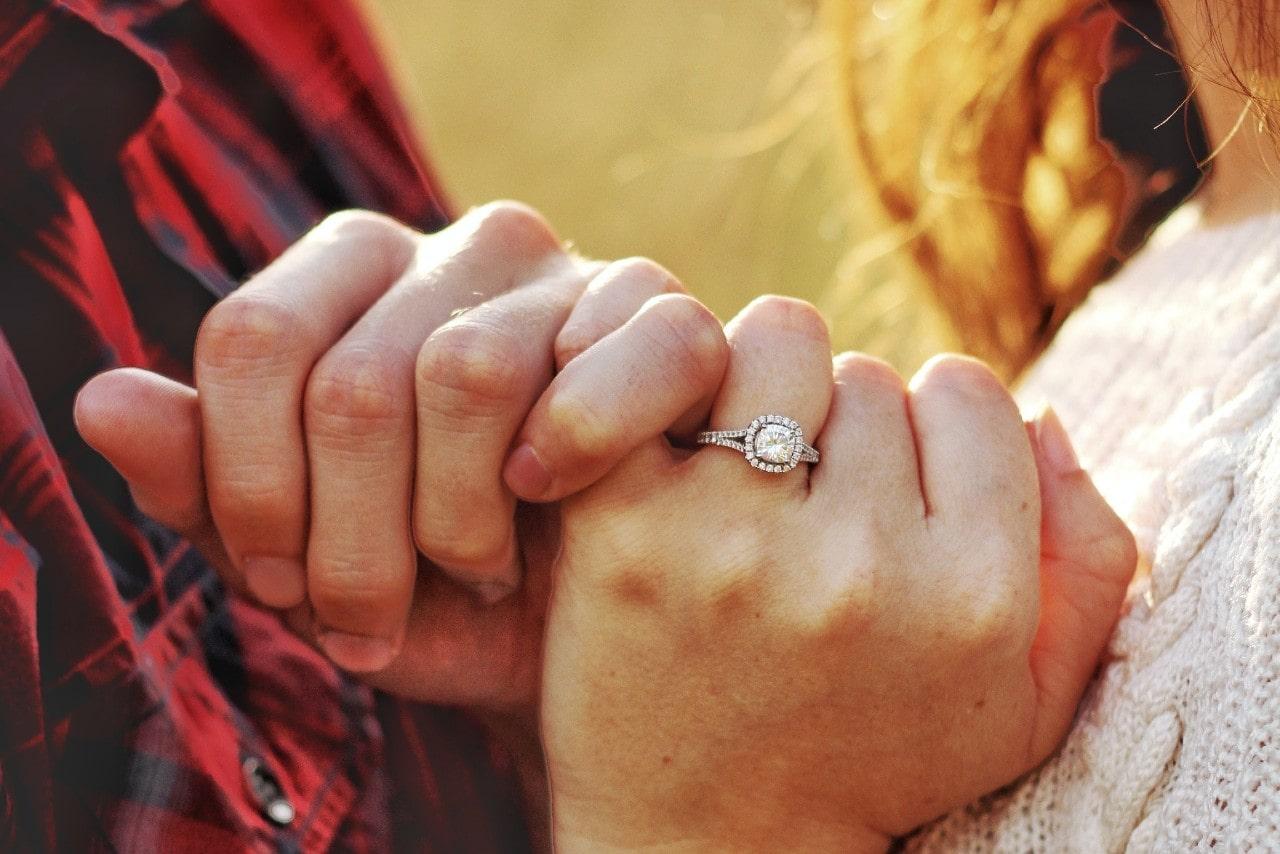 A couple intertwining pinkies, the woman wearing a halo, split band engagement ring.
