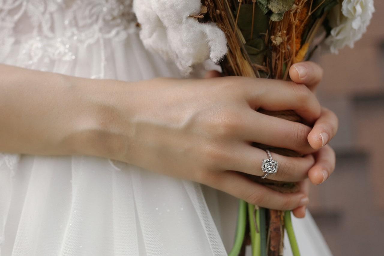 A bride holding her bouquet and wearing a halo, emerald cut diamond engagement ring. A bride holding her bouquet and wearing a halo, emerald cut diamond engagement ring.