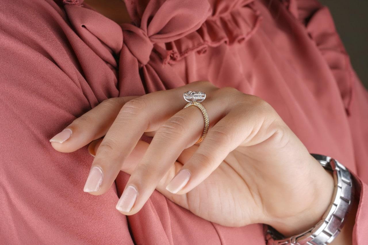 Close up image of a woman wearing a yellow gold, diamond engagement ring and a pink blouse.