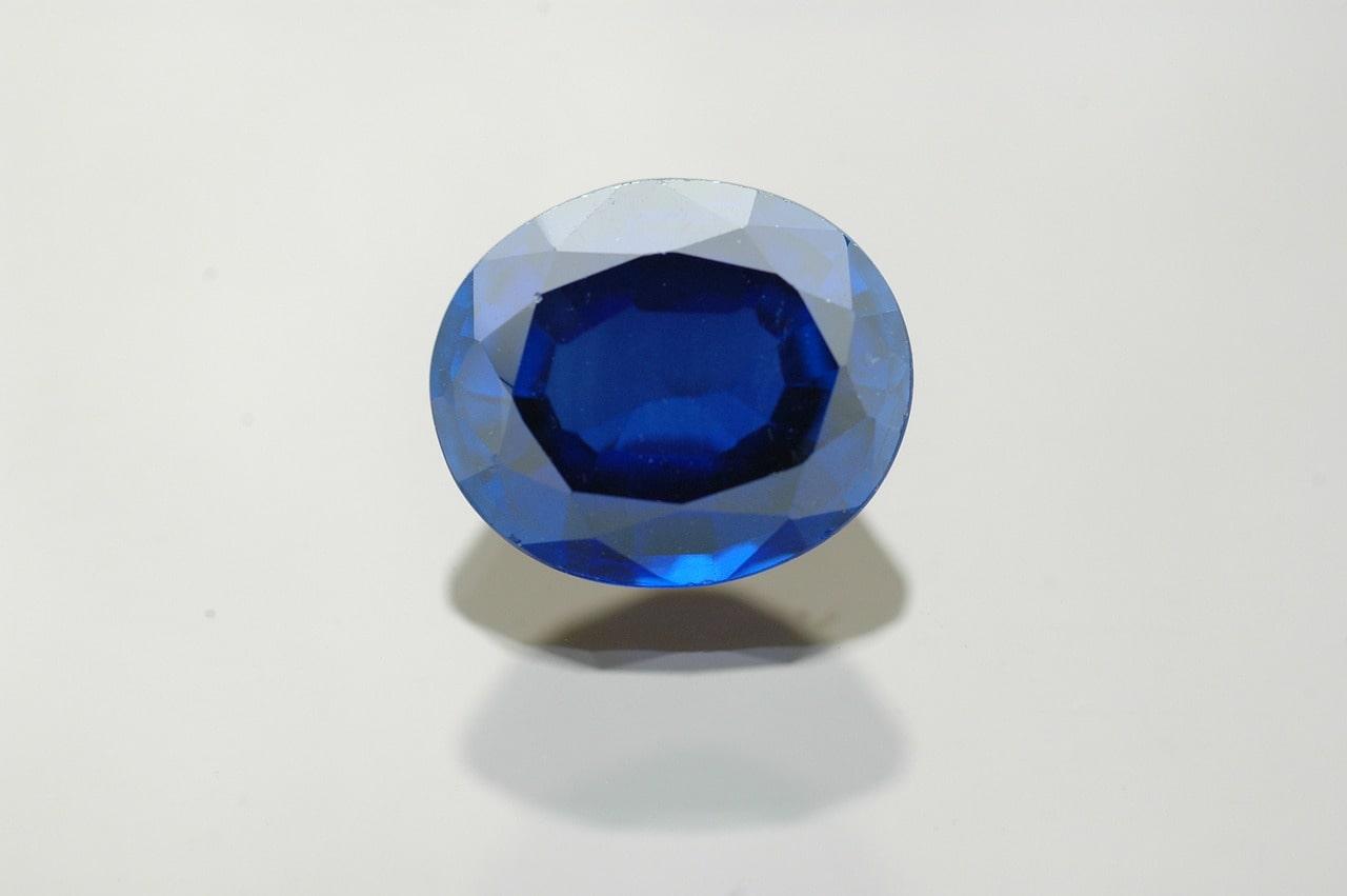 A close-up of an oval cut sapphire on a white surface. A close-up of an oval cut sapphire on a white surface.