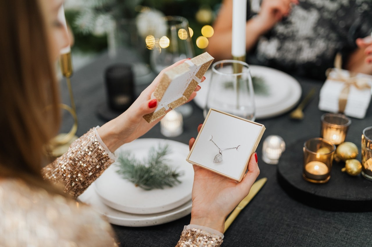 a woman opening a box containing a diamond necklace at a lavishly set table