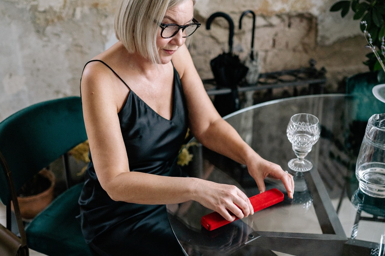 a woman at glass table opening a red necklace box
