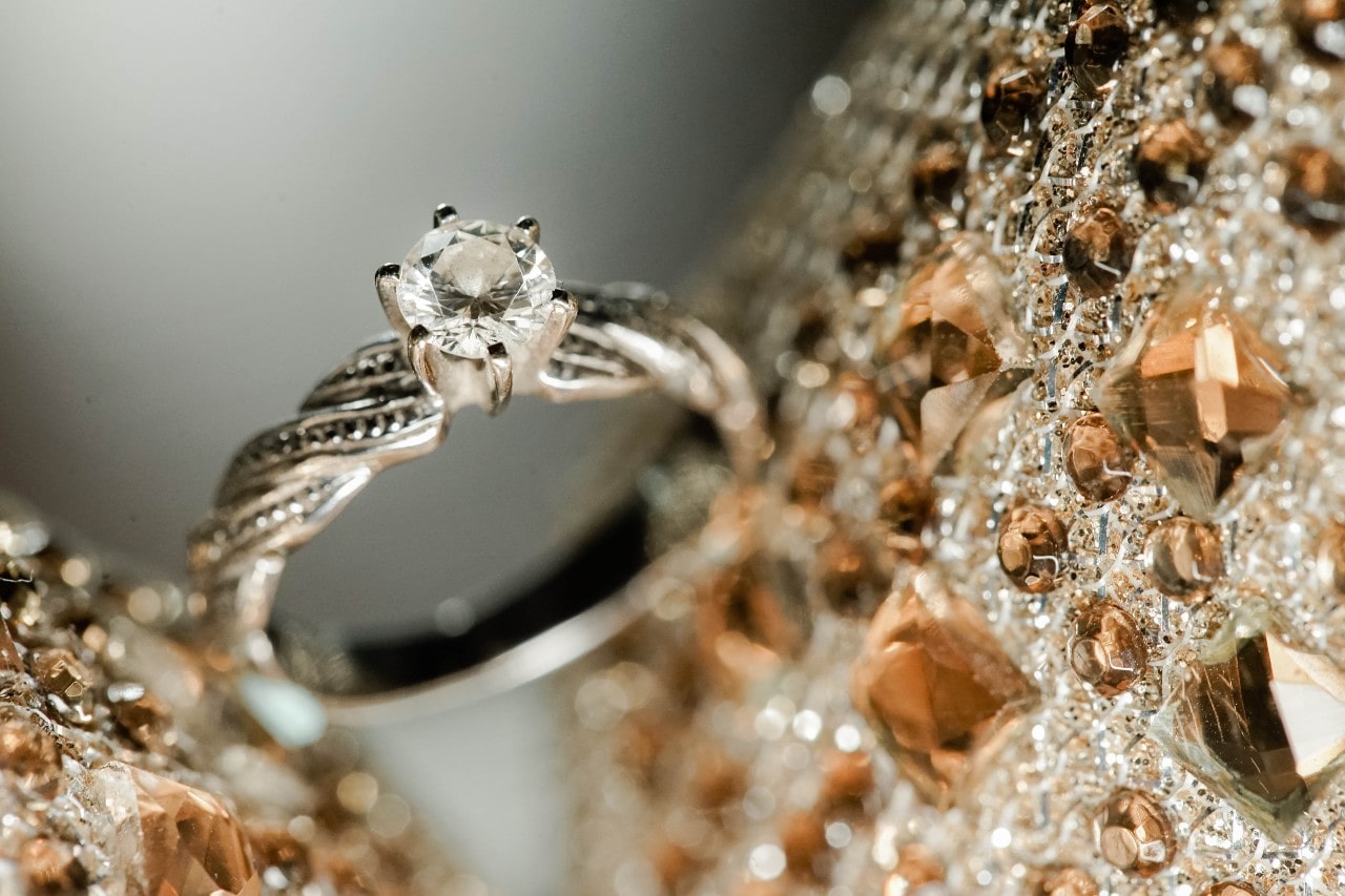 A close-up of a vintage-style engagement ring displayed in lavishly beaded fabric. A close-up of a vintage-style engagement ring displayed in lavishly beaded fabric.