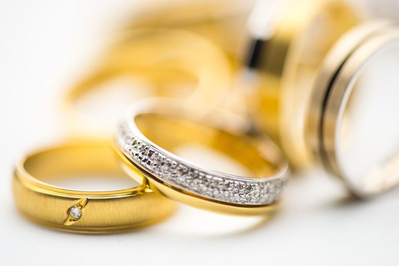 A close-up of a small selection of gold wedding bands, with a diamond accented ring front and center. A close-up of a small selection of gold wedding bands, with a diamond accented ring front and center.