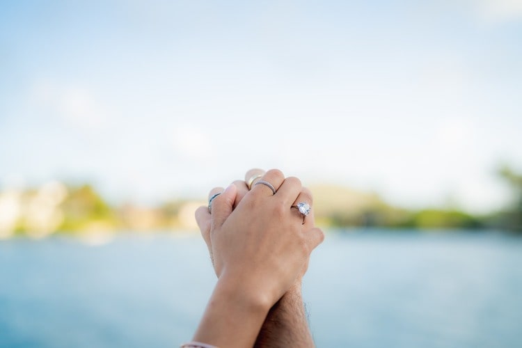 A couple holding hands together in the air, showing off the woman’s engagement ring