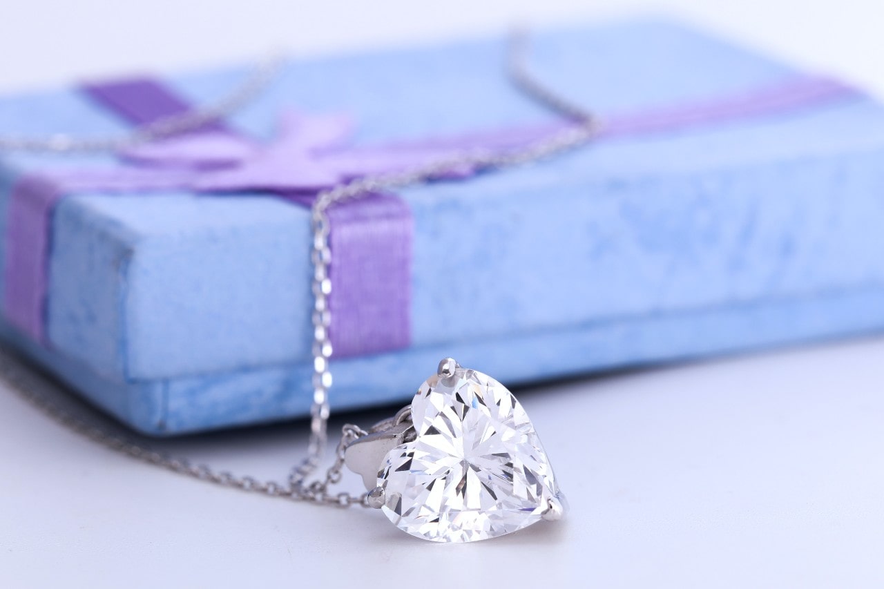 a heart shaped diamond necklace lying in front of a blue gift box