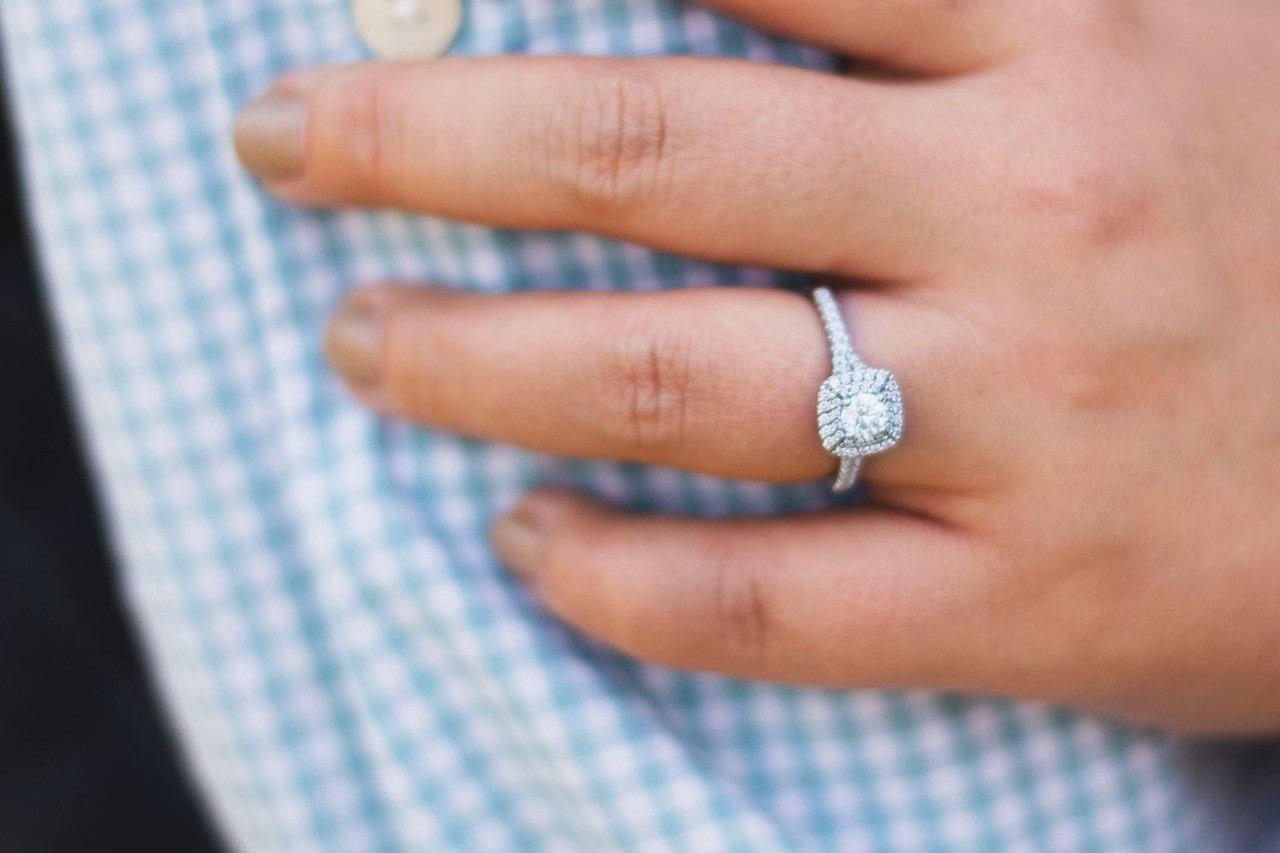 A woman with a halo princess cut engagement ring touches a man’s arm.