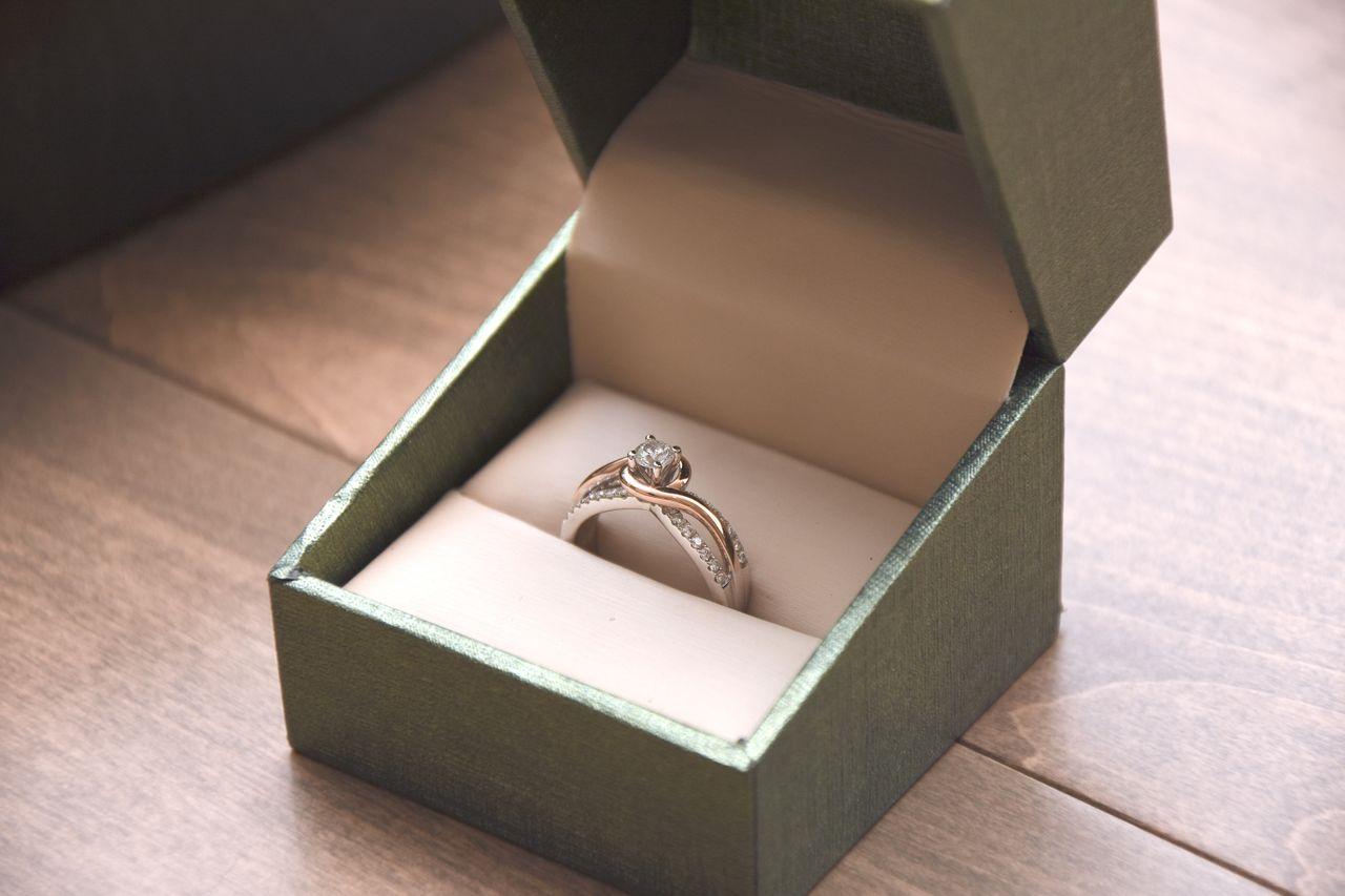 A modern-style engagement ring sits in a green ring box on a dinner table.