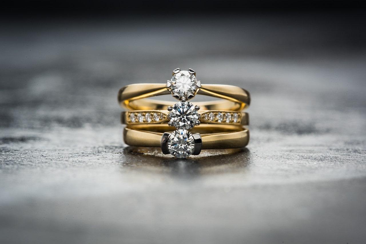 three yellow gold engagement rings sit on top of each other on a black background.