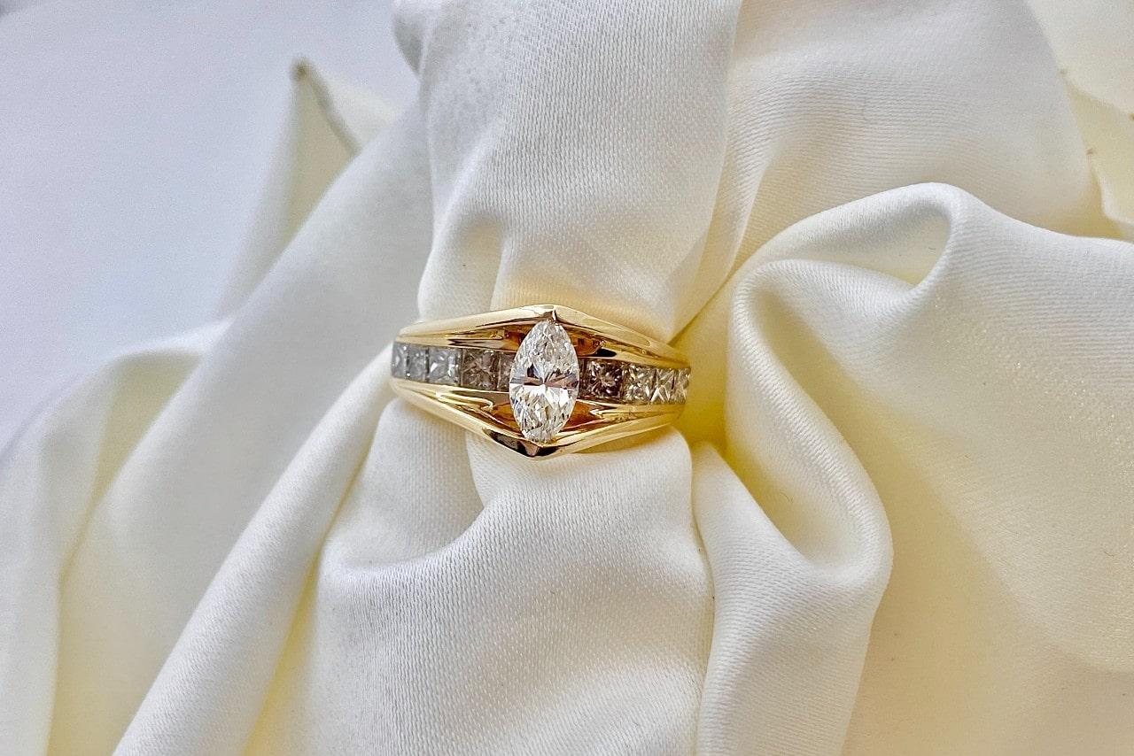 A marquise cut diamond with channel set princess cut diamonds in a bold yellow gold engagement ring displayed with arranged fabric