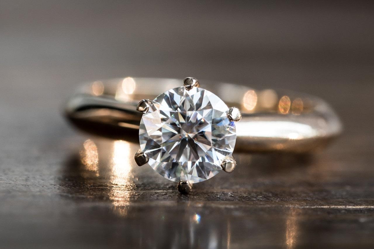 Focus on the a round cut diamond center stone on a yellow gold solitaire ring laying on its side on a polished wood table