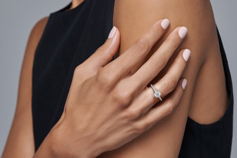 A close up of a round cut diamond side stone ring on the hand of a woman