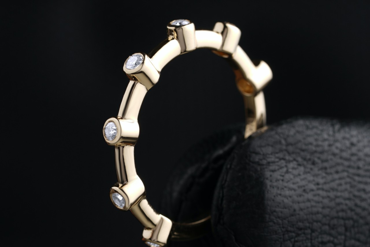 a yellow gold wedding band with bezel set diamonds held by a gloved hand