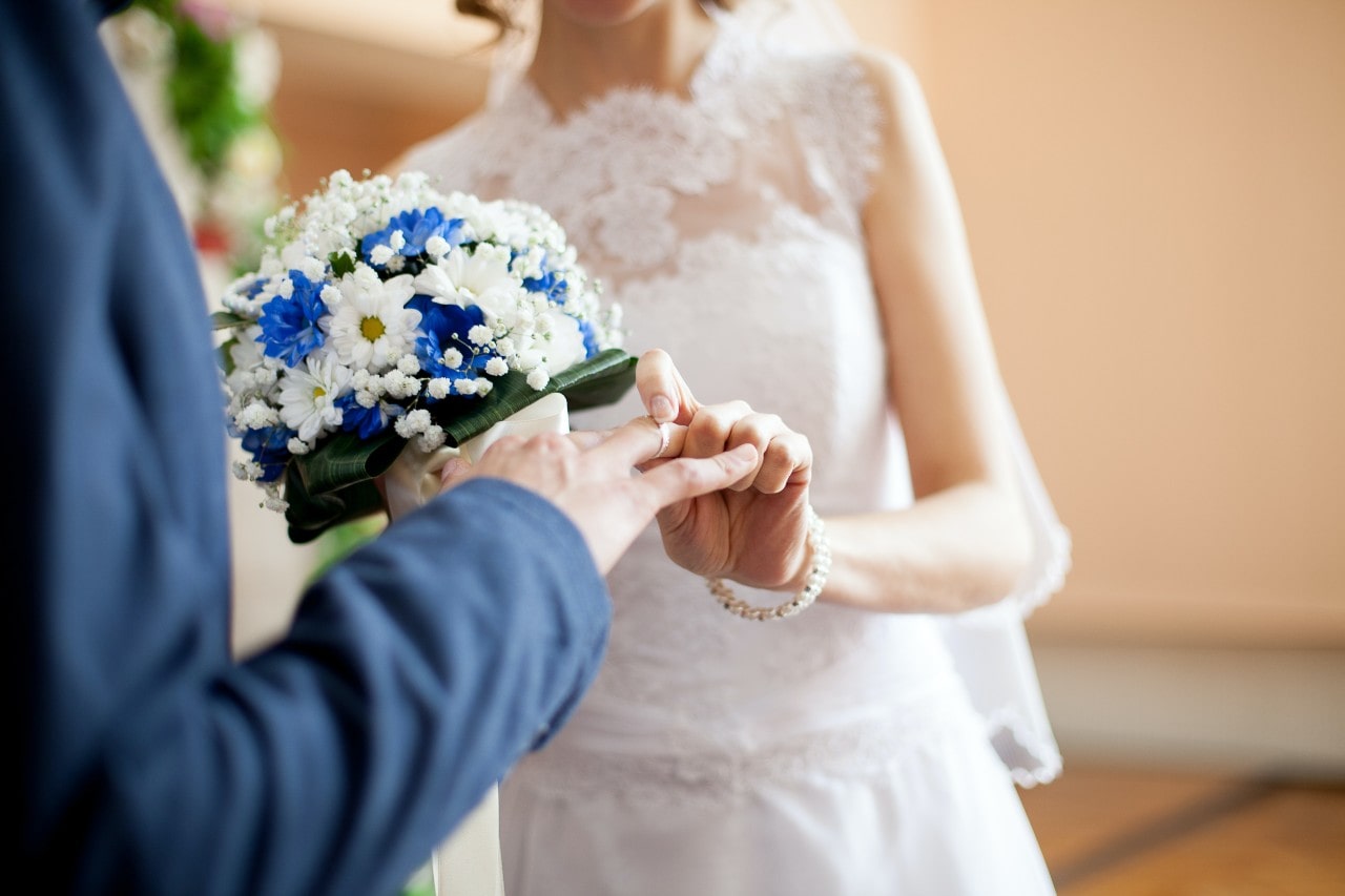 a bride placing a wedding band on her grooms finger at the altar